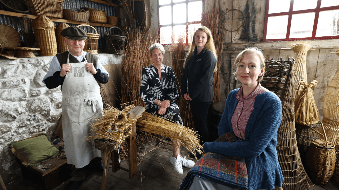 Costumed makers who work the Ulster Folk Museum, showing traditional heritage skills of printing and weaving pictured inside the authentic basket maker's workshop with willow creations on display. Representatives from the museum and CITB NI are standing in the middle with the costumed guides either side. 