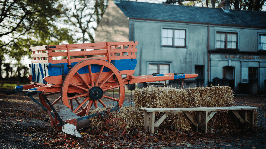 Hay bales and a bench, with an orange and blue cart sitting
