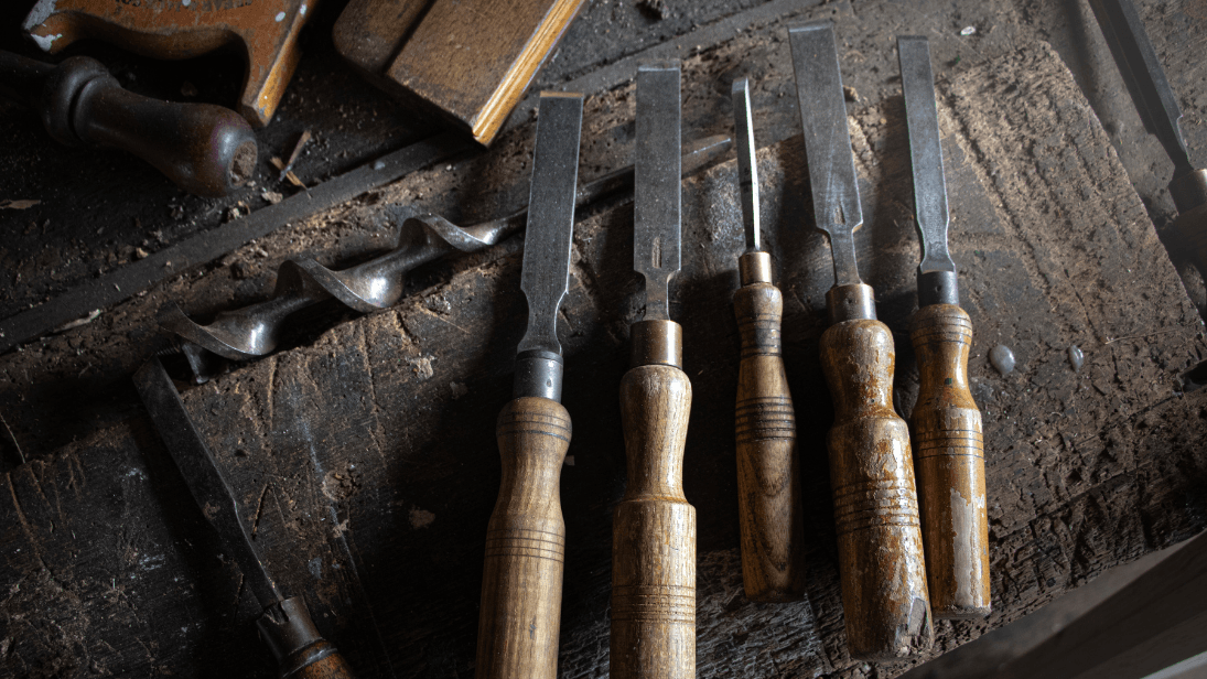 A series of chisels lay across a workbench.