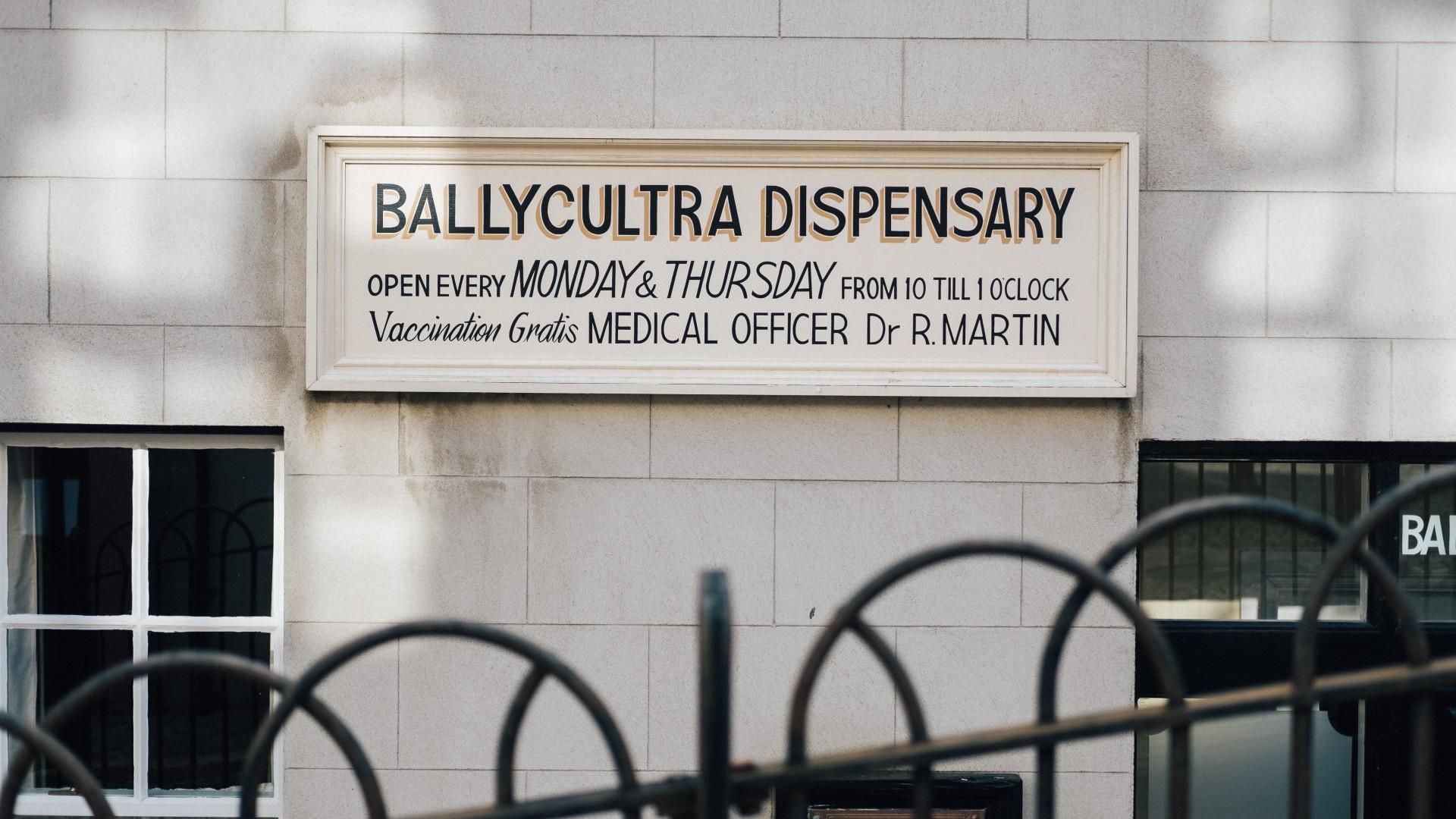 A hand-painted pharmacy sign reading 'Ballycultra Dispensary, open every Monday and Thursday' giving the name of the doctor and opening hours.