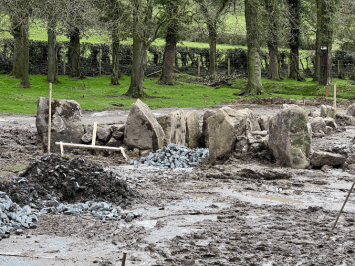 A muddy field has been excavated and large stones are buried in the ground.