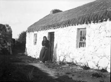 Shawled woman at doorway of rope thatched house, black and white photograph