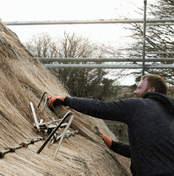 A man places a peg to hold new thatch in place.