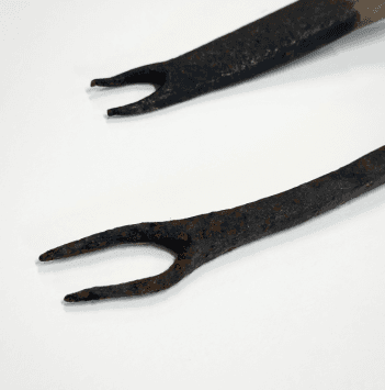 Two thatching forks lie on their sides. The prongs of one are longer, while the one has shorter and more worn prongs.