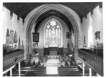 A wide shot of a church interior, with a focus on the stained glass window in the background.
