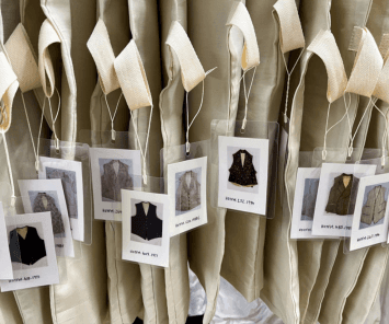 A row of waistcoats wrapped in white covers with labels dangling outside.