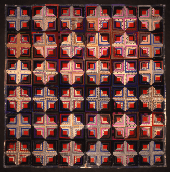 A dark-coloured patterned quilt, with lots of cross, diamond and square patterns.