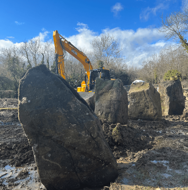 Standing stones in the foreground while in the background a yellow digger stands. 