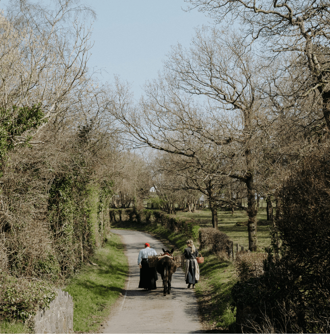 Two women in old fashioned clothing walking with a donkey in the countryside