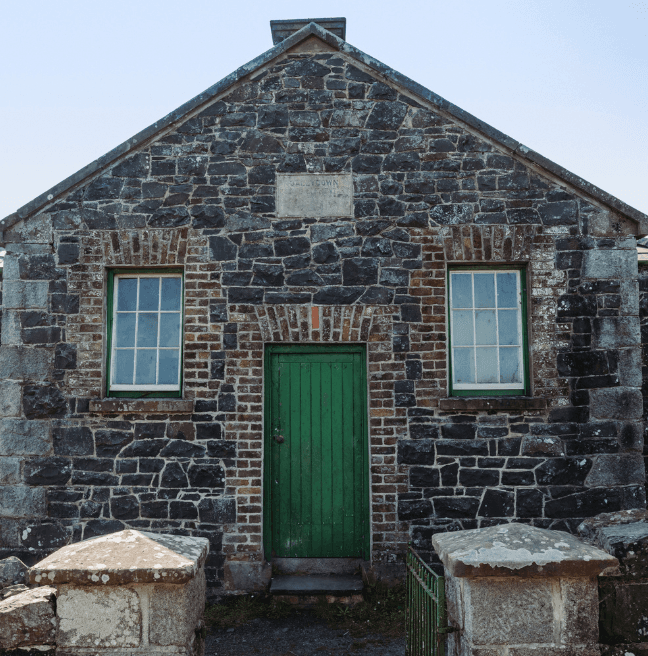 A stone school with a green door stands in the sunshine