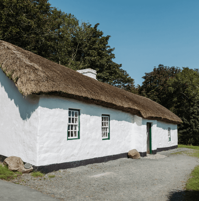 A whitewashed thatched cottage sits in the sunlight.