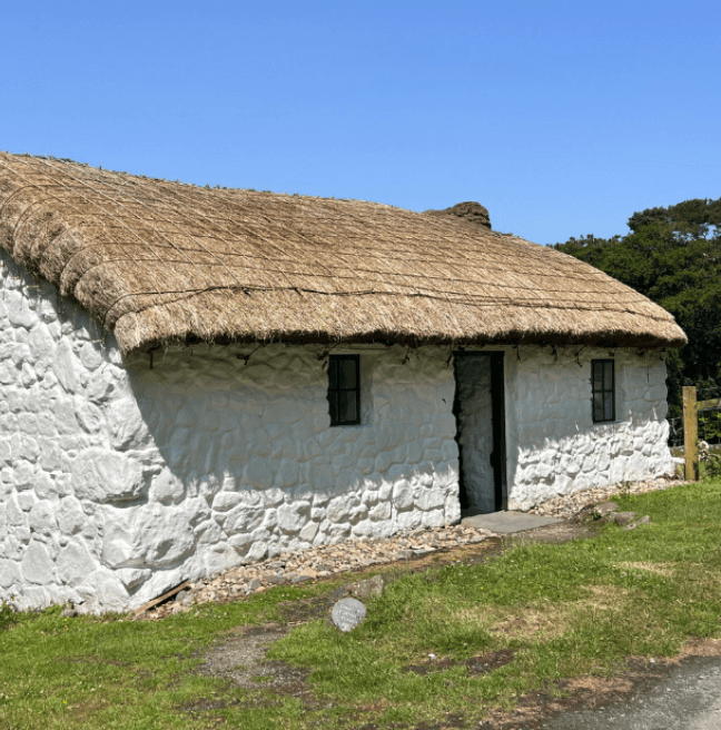 A whitewashed cottage with a thatch roof on a sunny day.