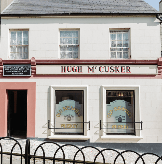 A two storey building hosting a pub. The name Hugh McCusker is painted above the downstairs frosted windows.