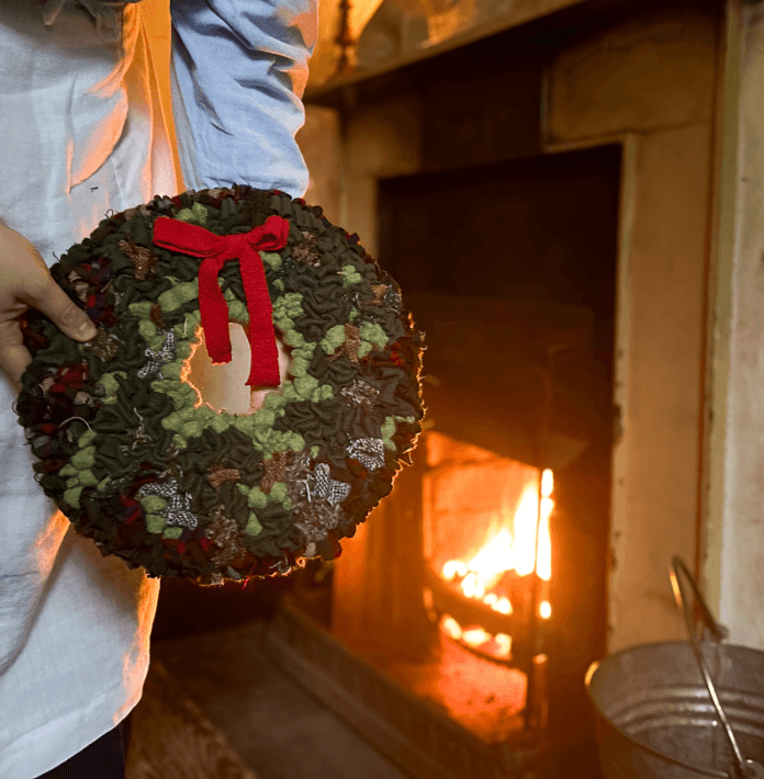 A woman holds a rag wreath in front of a warm open fire. 