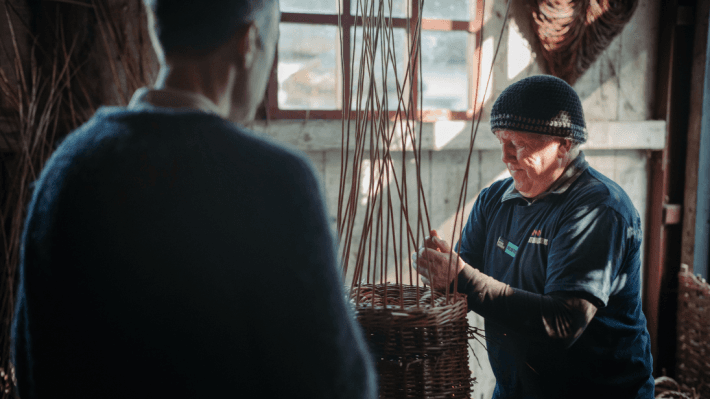 a man volunteering at the folk museum by helping with basket weaving