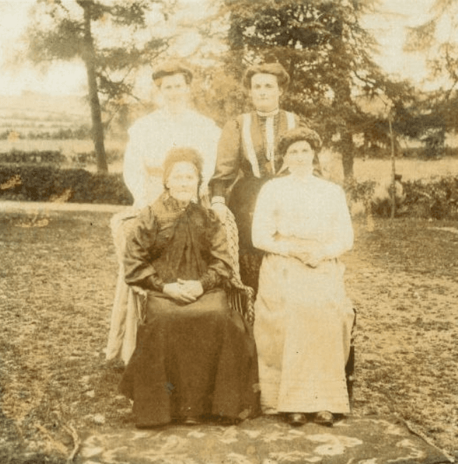 Old fashioned black and white image of four women posing for a photograph, two standing behind two seated