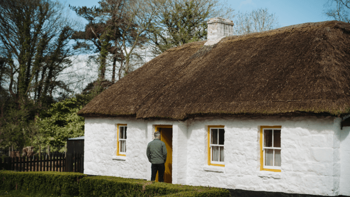 A man  walking inside a white thatched cottage at the folk museum