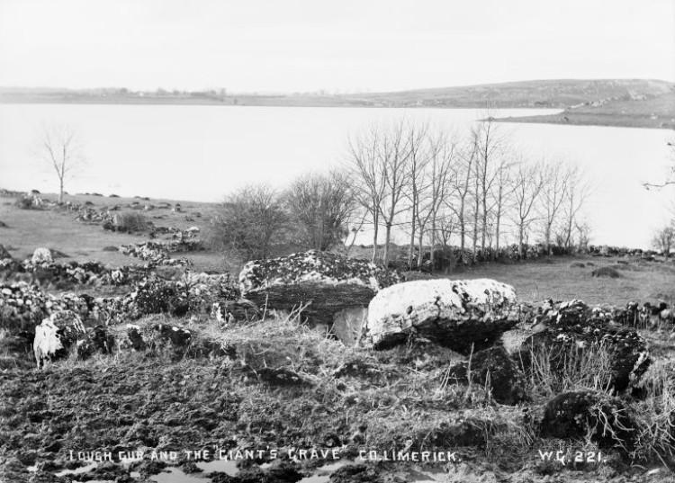 An archaeological monument sits on a hillside beside a lough.