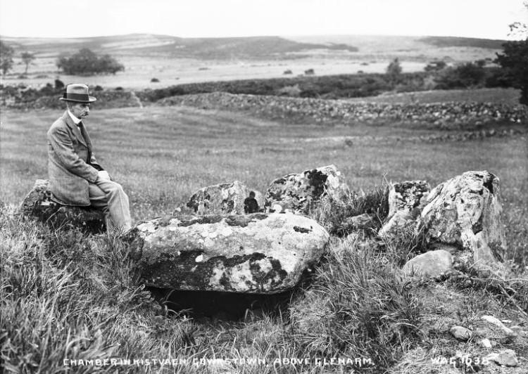 A man sits on a stone overlooking an archaeological monument.