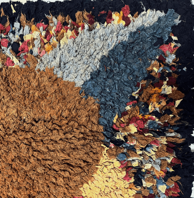 A detail of a rug with an oval centre, light and dark blue triangle, black trim, and multicoloured backgroud.